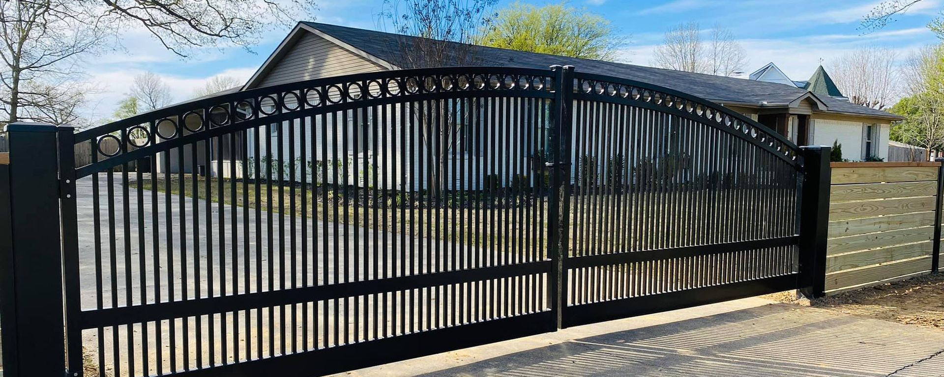 A black gate is open to a driveway in front of a house.