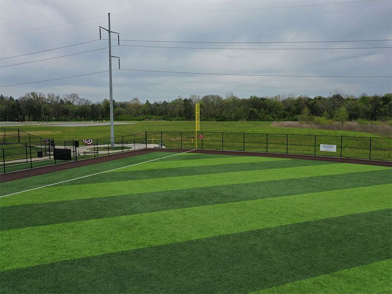 A baseball field with a fence around it and a field in the background.