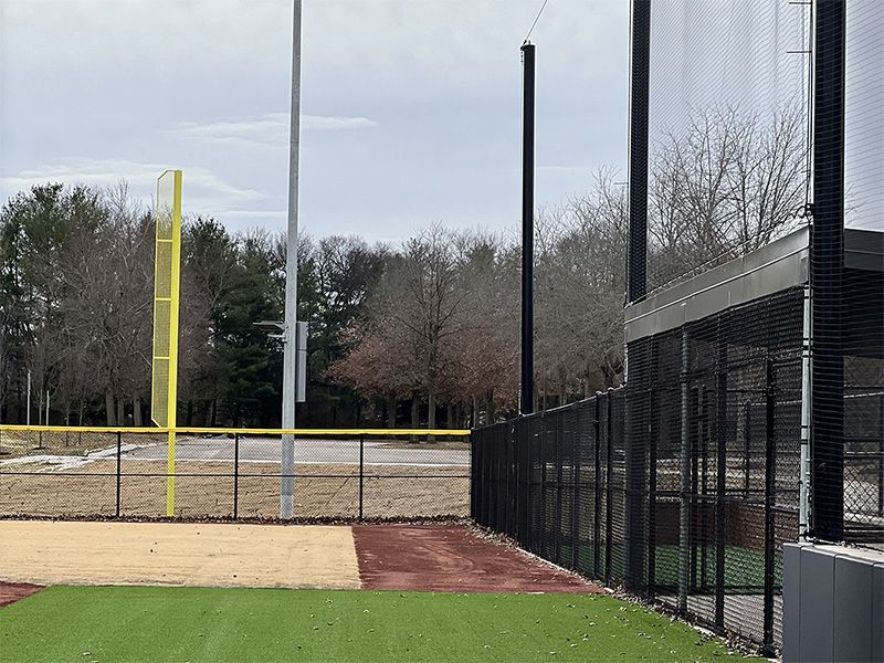 A baseball field with a fence and trees in the background.