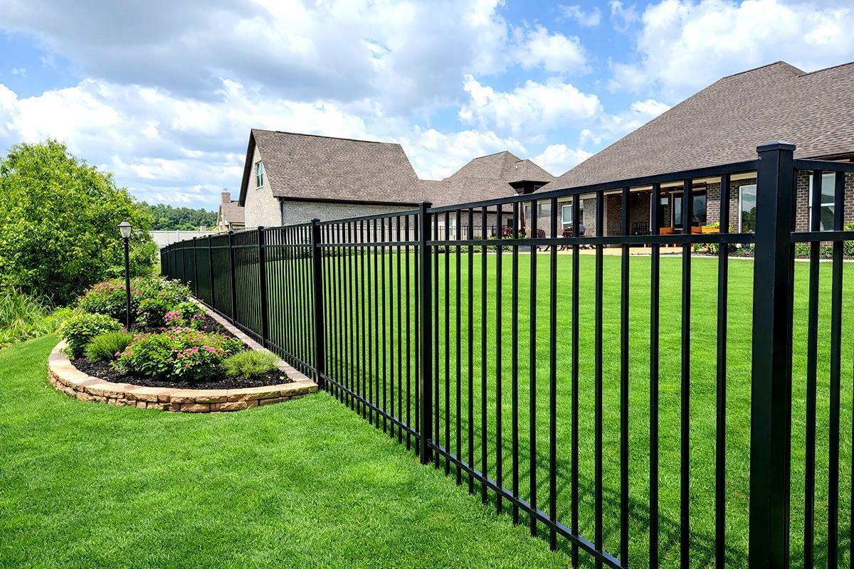 Black metal fence bordering green lawn, with a house and sky in the background.