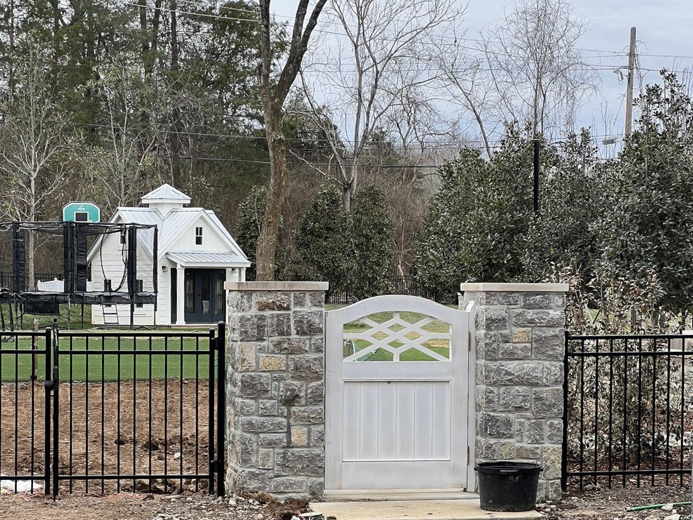 A white gate is surrounded by a stone wall and a black fence.