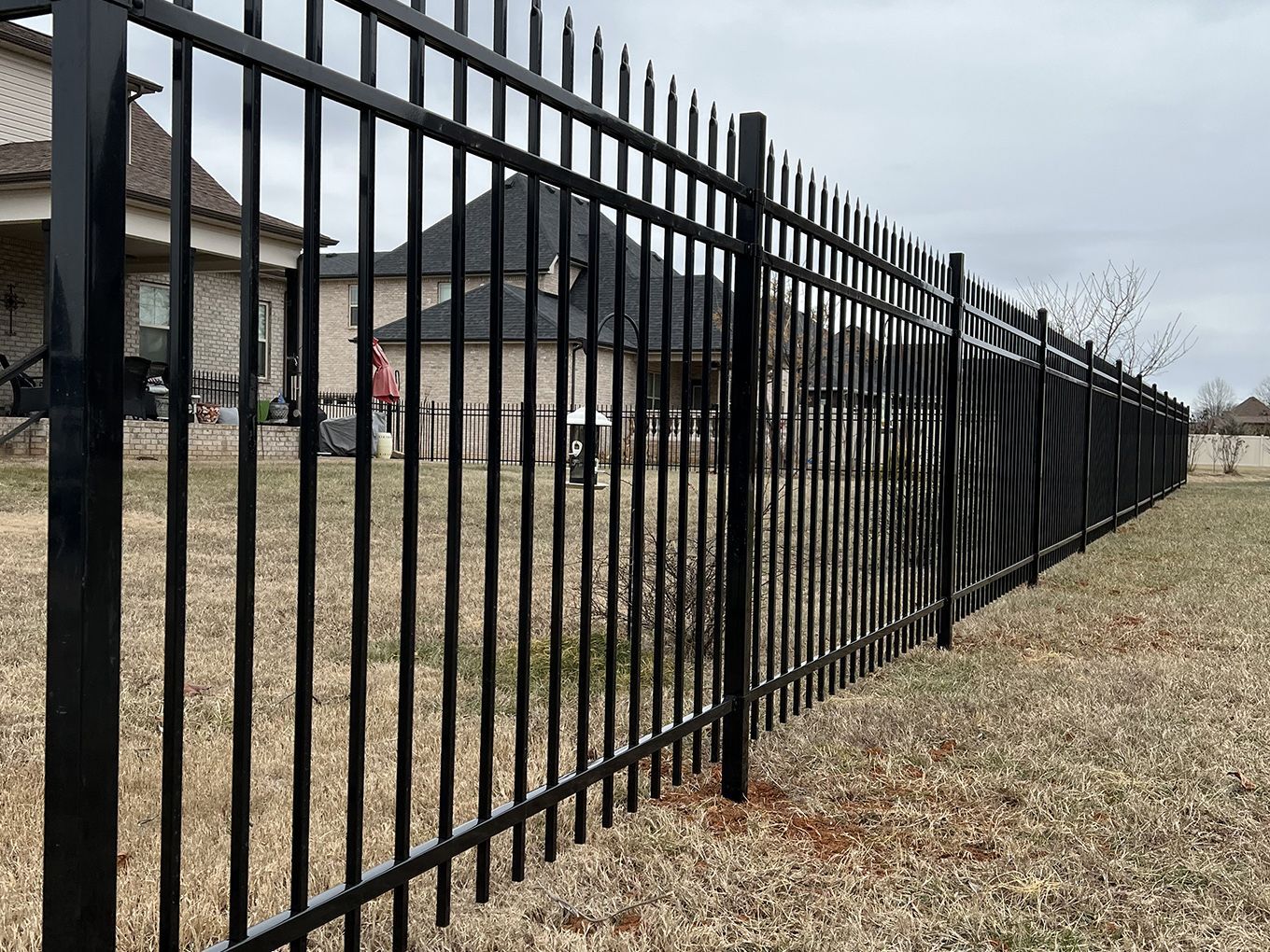 A black metal fence surrounds a grassy field in front of a house.