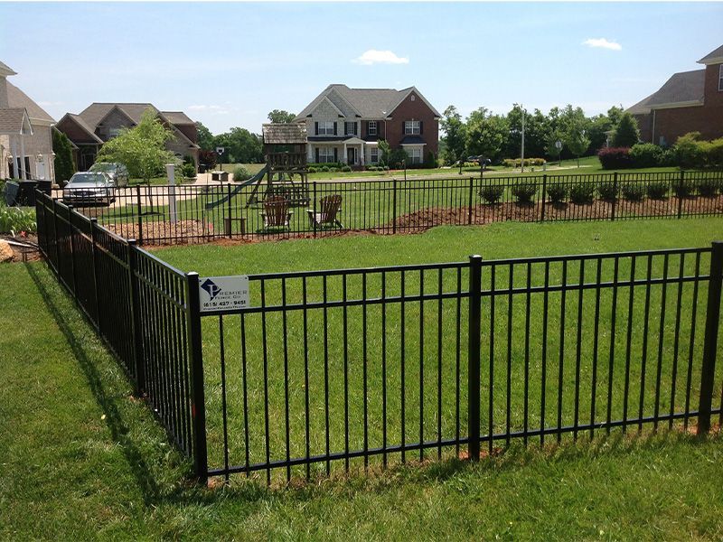 A black metal fence surrounds a lush green yard