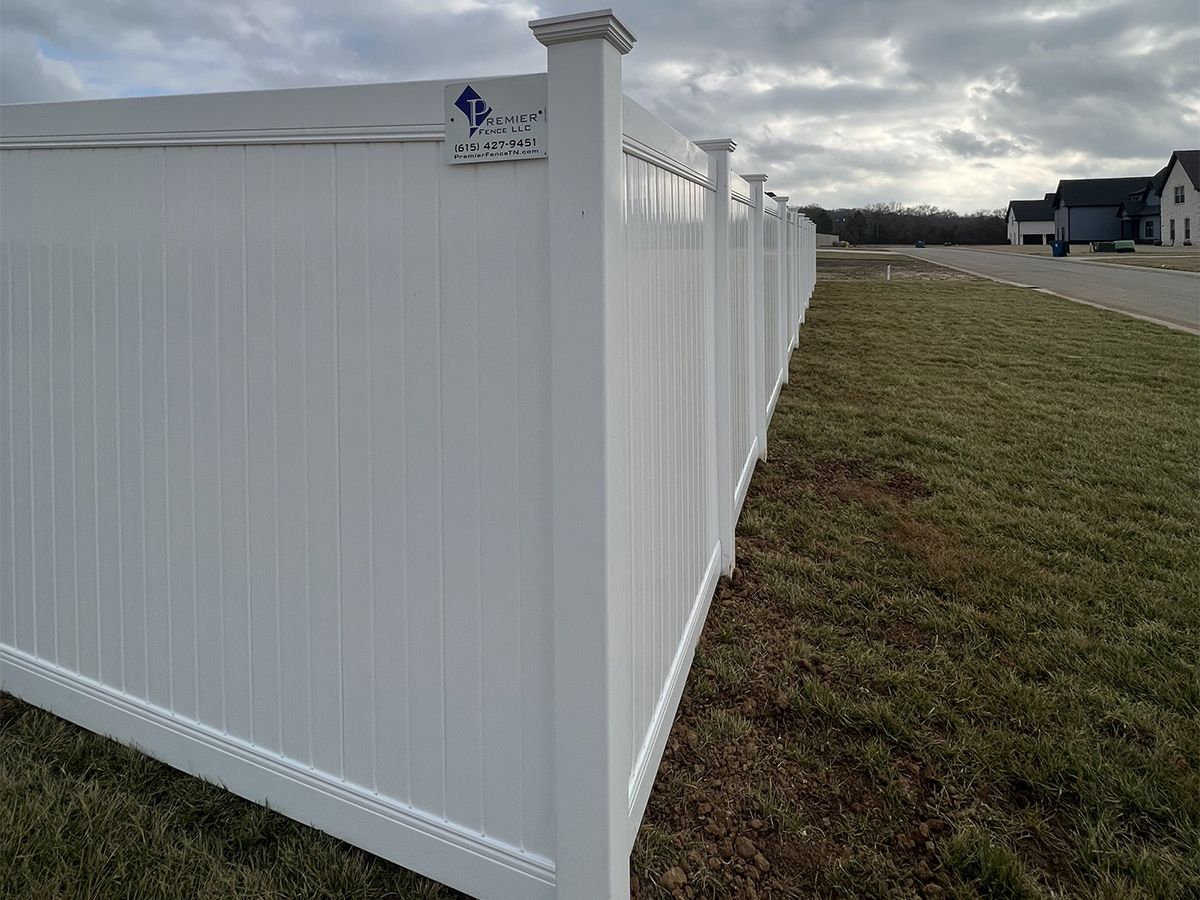 A white vinyl fence is sitting in the middle of a grassy field.