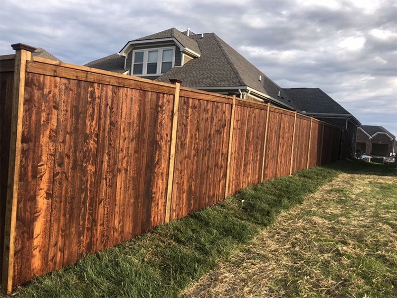 A wooden fence surrounds a grassy field in front of a house.