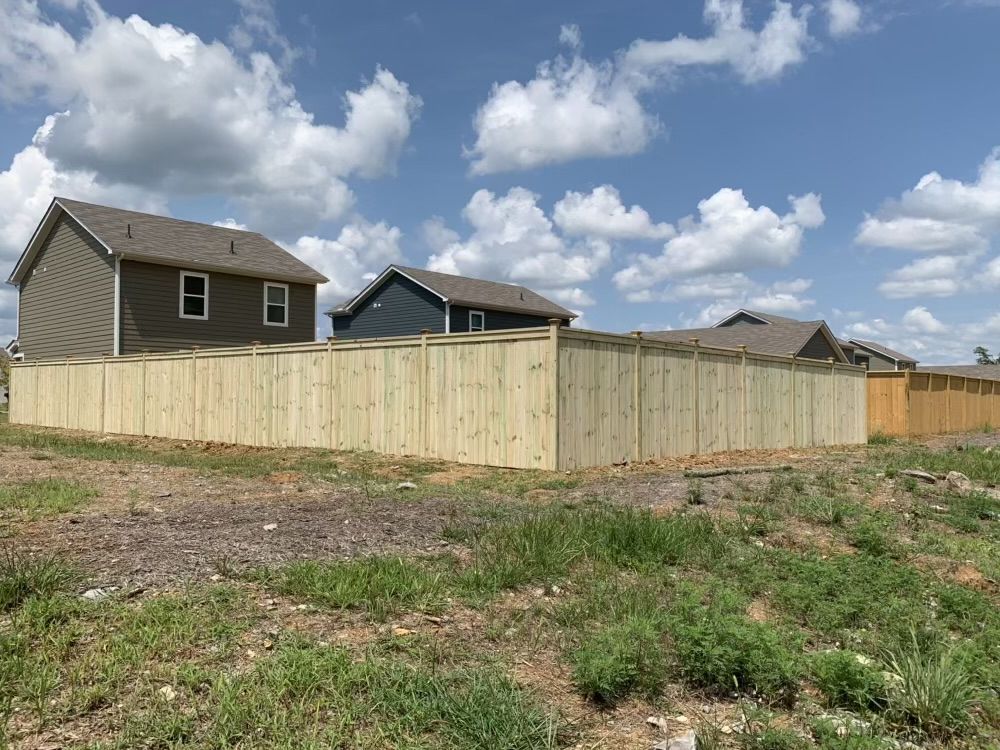 A wooden fence surrounds a residential area with houses in the background.