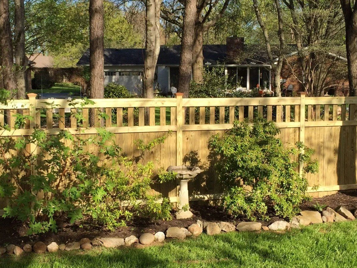 A wooden fence surrounds a lush green yard in front of a house.