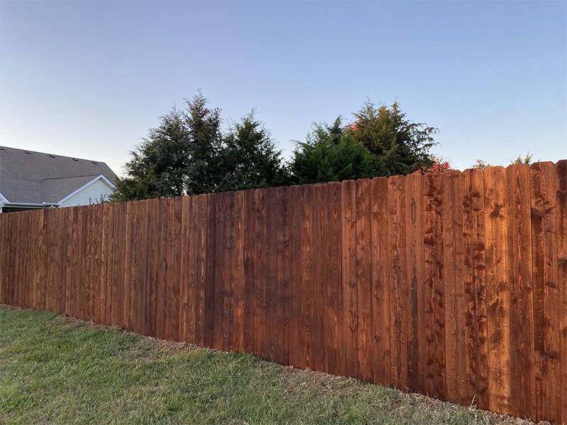 A wooden fence is surrounded by grass and trees in a backyard.