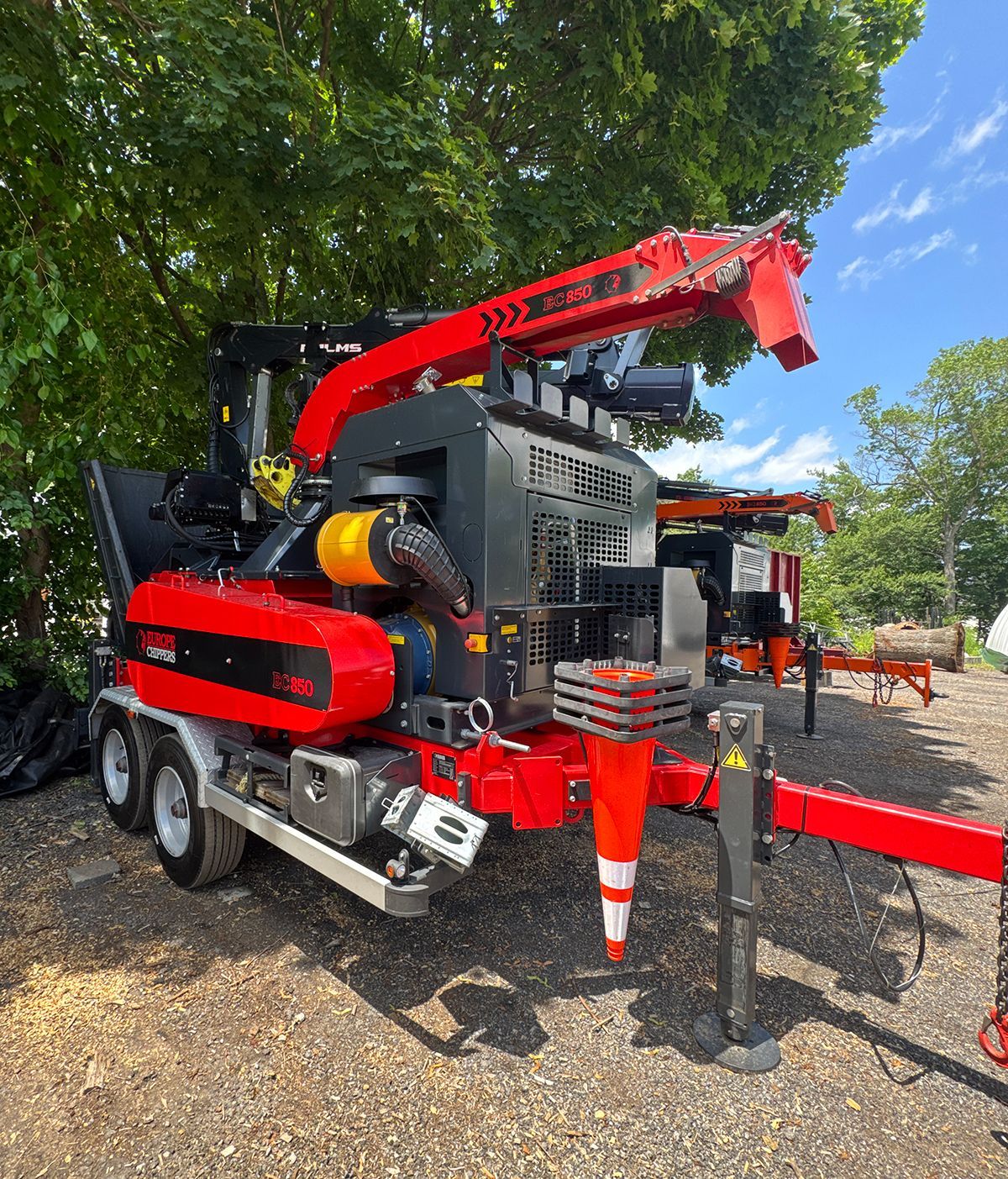 Red and black wood chipper with a crane arm on a trailer, parked outdoors.