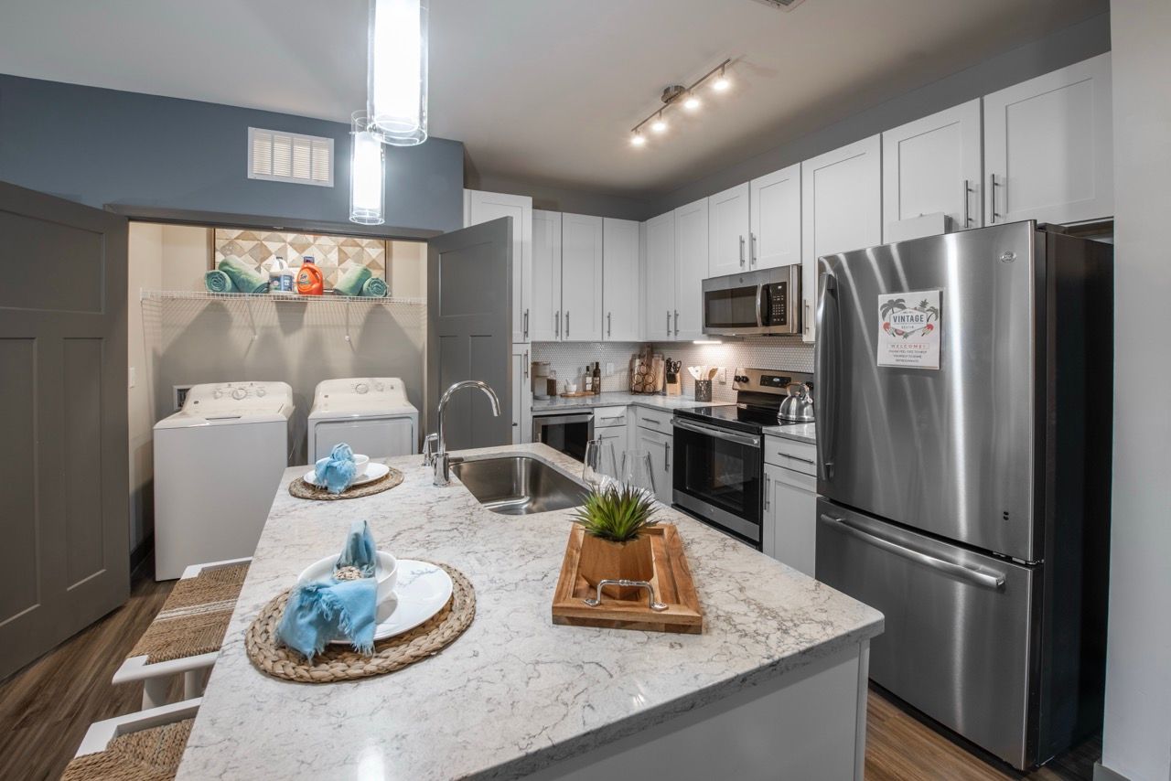 Open kitchen with marble island, stainless steel appliances, and a visible laundry area.