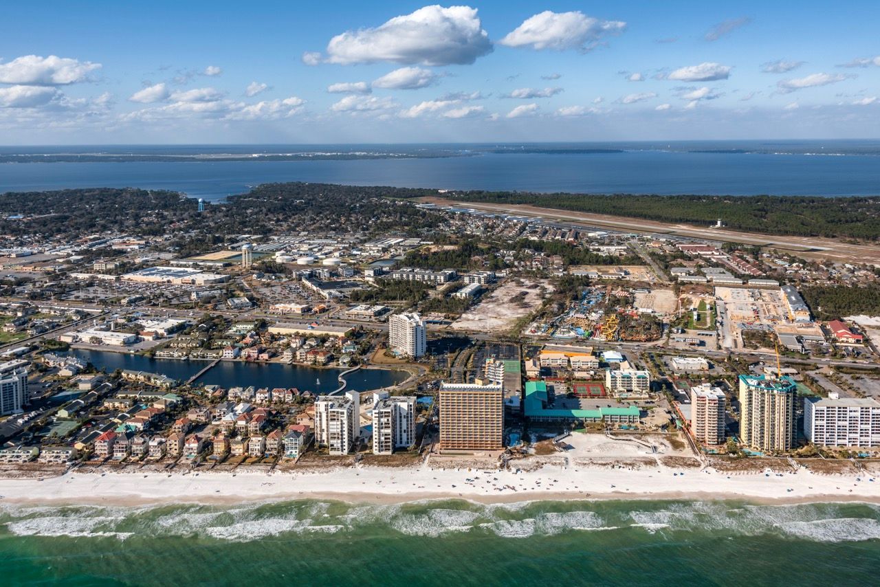 Aerial view of a coastal city with a beach, water, and high-rise buildings along the shoreline.