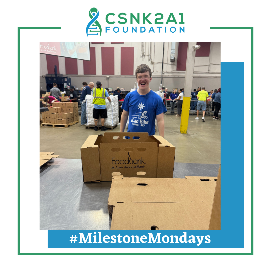 A person smiling at a food bank, assembling cardboard boxes. The scene is brightly lit.