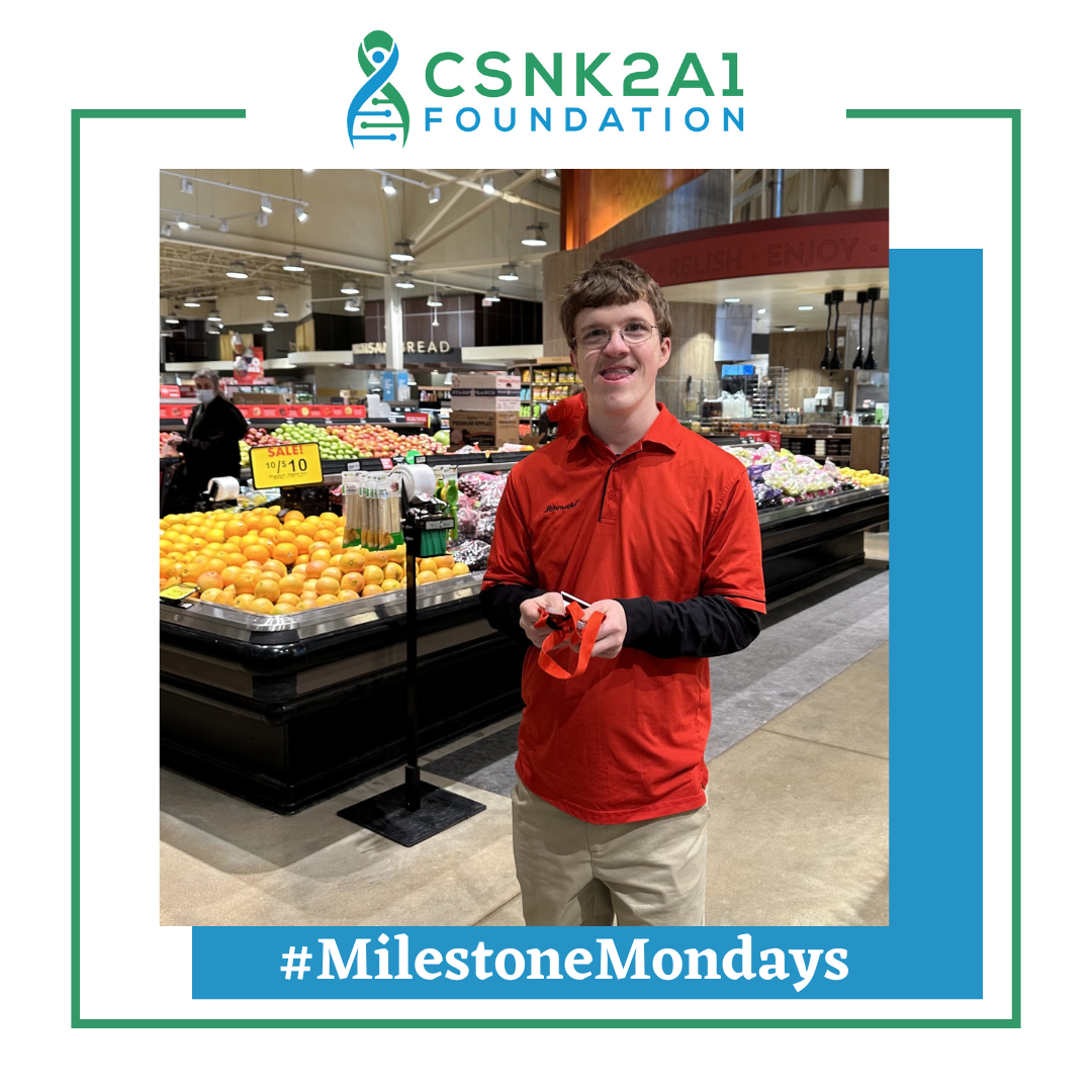 Man in red shirt holding object, smiling in grocery store. CSNK2A1 Foundation logo, #MilestoneMondays.