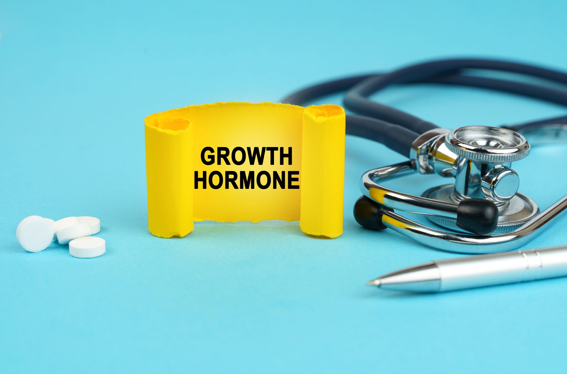 A stethoscope, pen, pills and a yellow sign that says growth hormone.