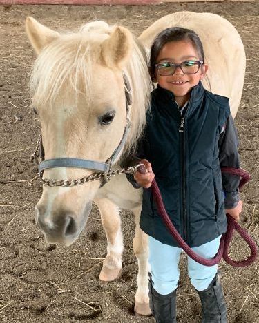 A little girl is standing next to a white horse on a leash.
