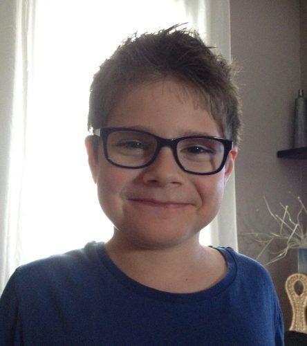 A young boy wearing glasses and a blue shirt is smiling for the camera.