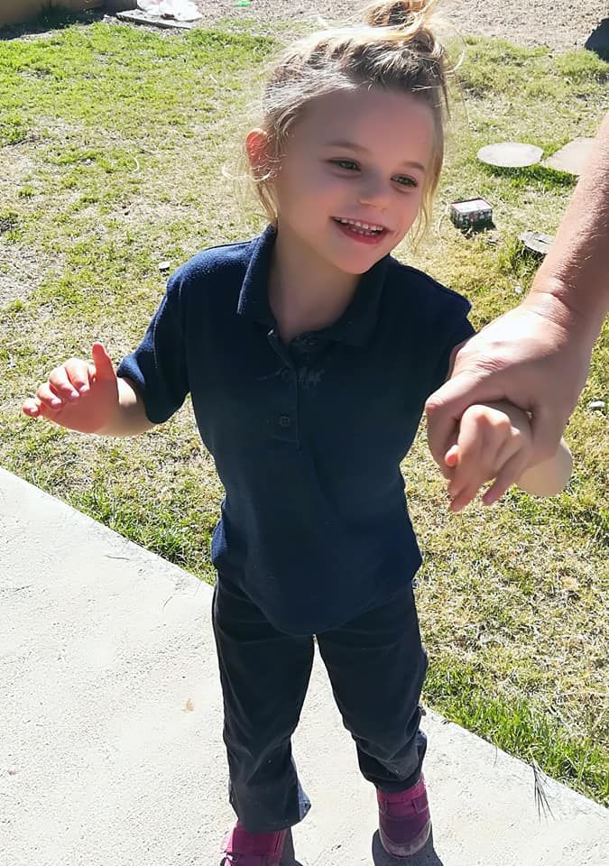 A child in a dark polo shirt and black pants is standing on concrete.