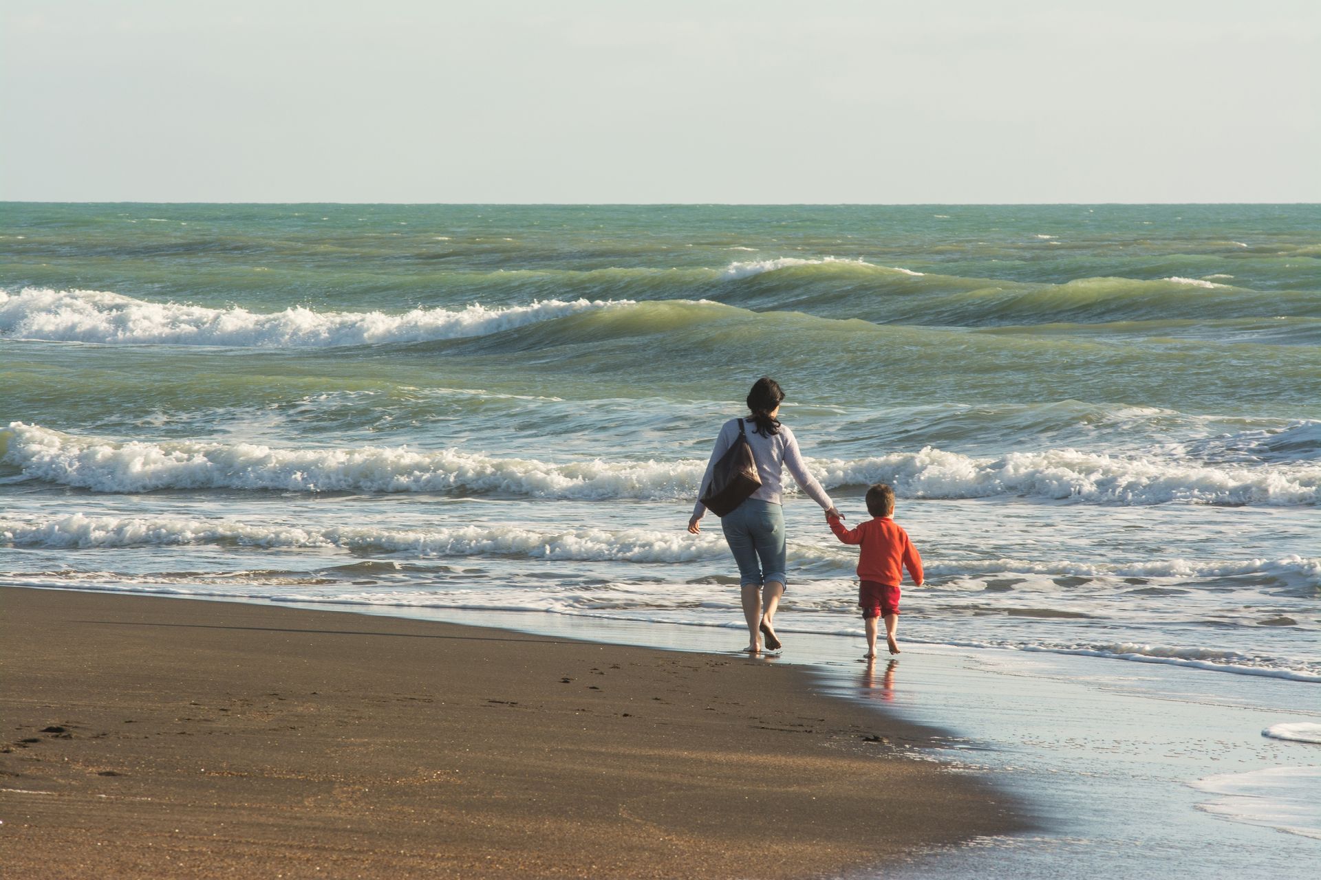 A woman and child are walking on the beach holding hands