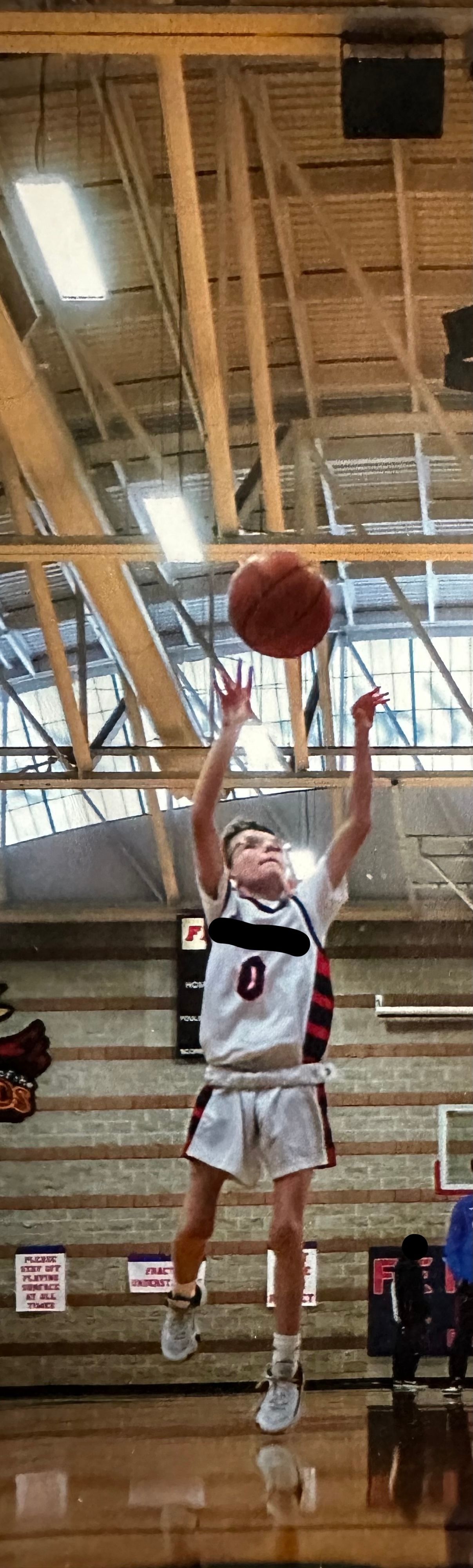 A basketball player is jumping in the air to catch a basketball in a gym.