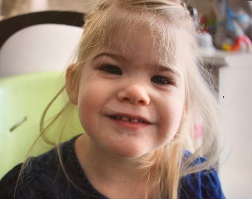 A little girl is sitting in a high chair and smiling at the camera.