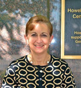 A woman in a black and gold polka dot shirt is smiling in front of a sign.