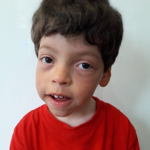 A young boy in a red shirt looks at the camera