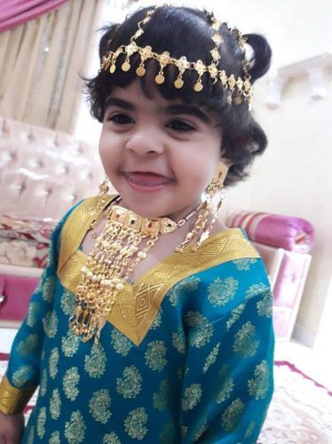 A little girl wearing a blue and gold dress and gold jewelry.