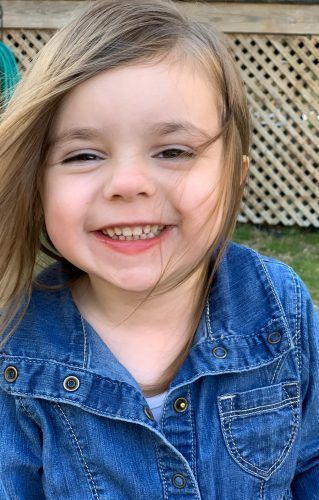 A little girl wearing a denim jacket is smiling for the camera.