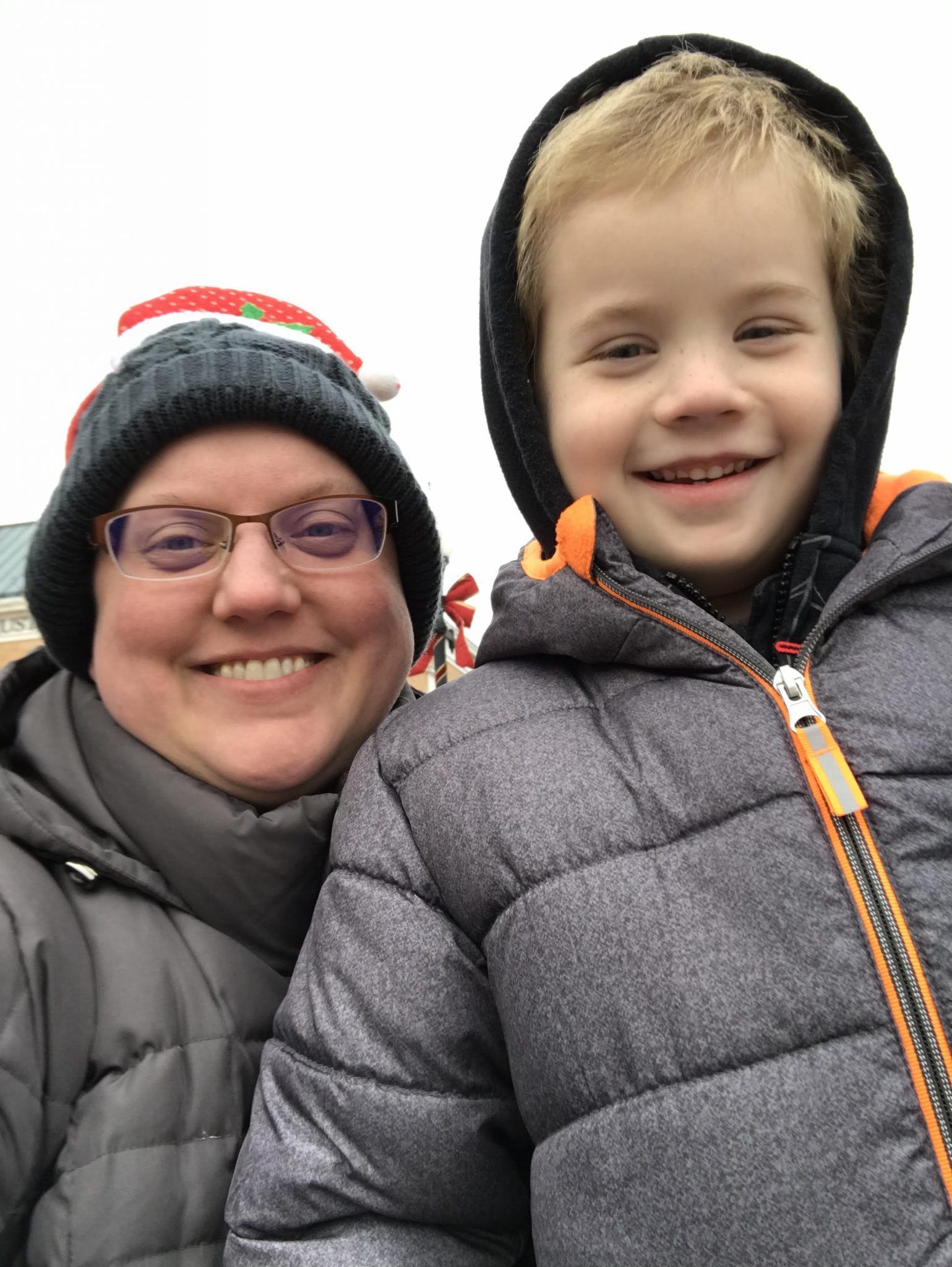 A woman and a boy are posing for a picture . the boy is wearing a santa hat.