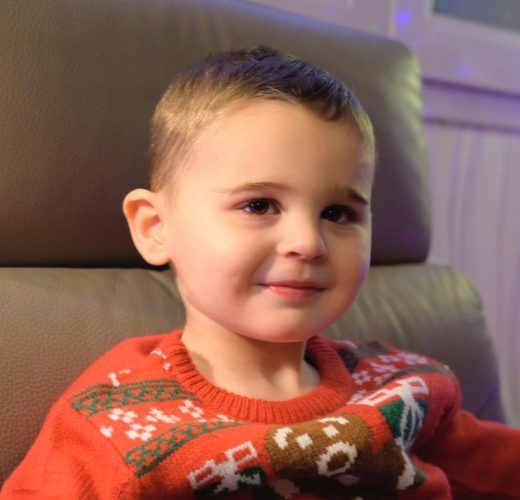 A little boy wearing a red sweater with a bear on it.
