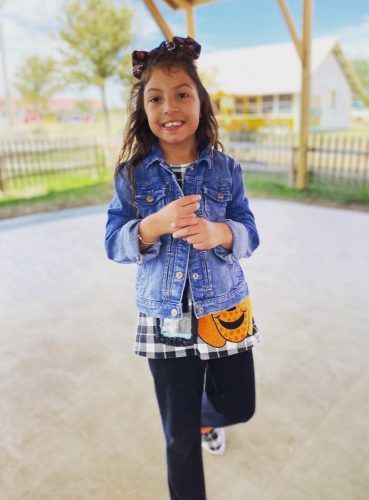 A little girl is wearing a denim jacket and a pumpkin skirt.