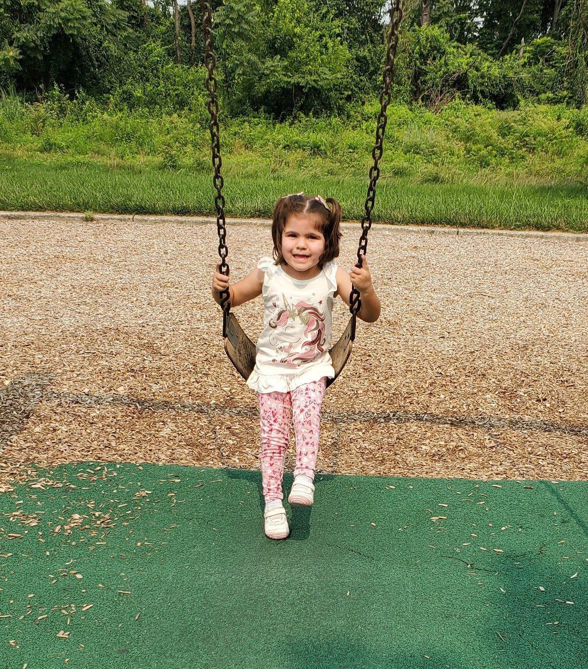 A little girl is sitting on a swing in a park.