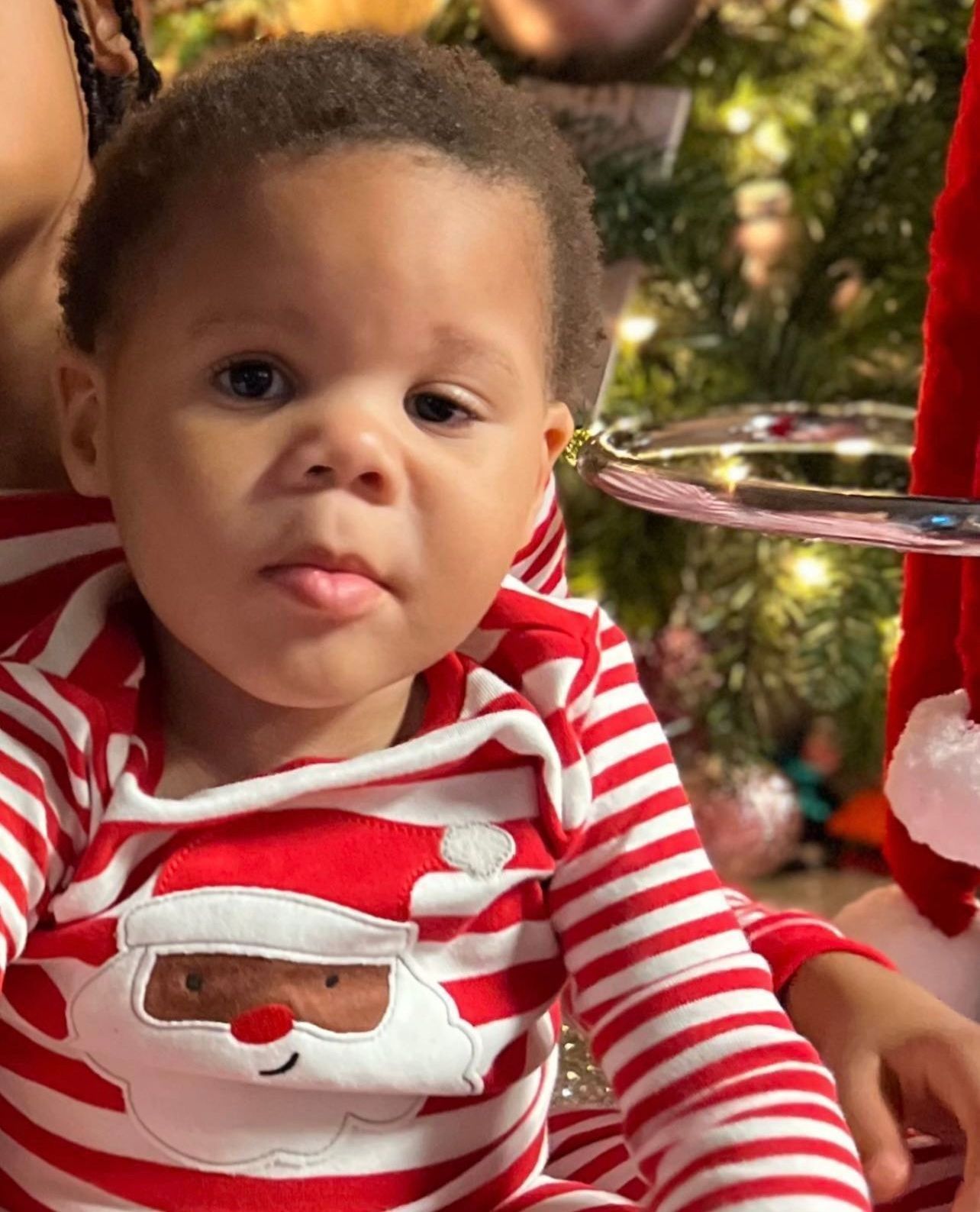 A baby in a santa outfit is sitting in front of a christmas tree.
