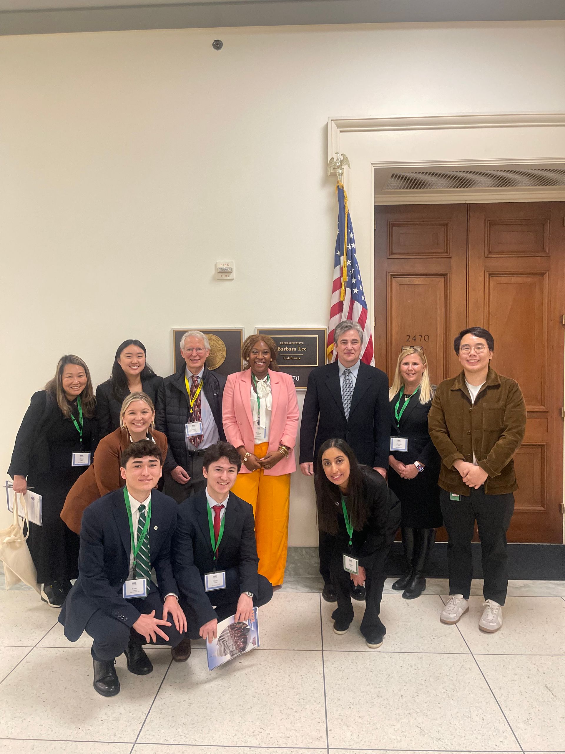 Group poses near American flag and plaque in a building hallway. People are smiling.