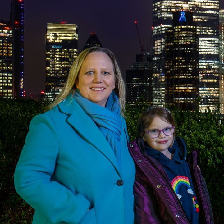 A woman and a little girl are posing for a picture in front of a city skyline at night.