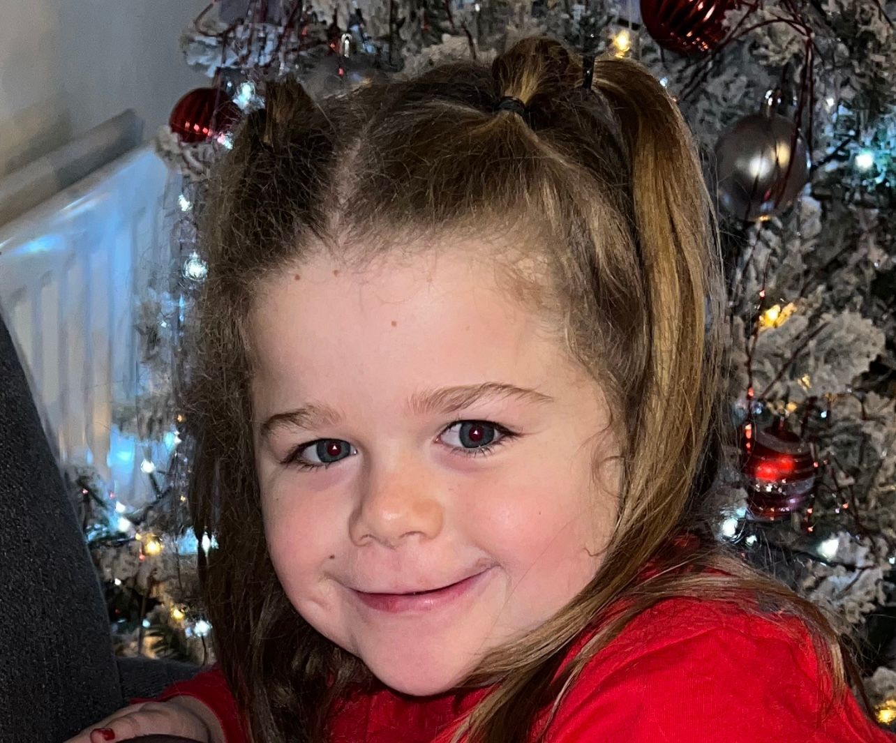 A little girl is smiling in front of a christmas tree.