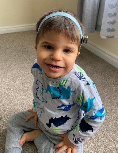 A little boy wearing a headband is sitting on the floor.