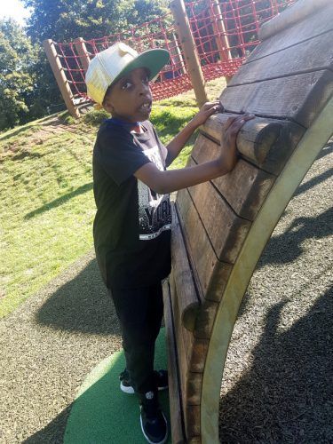 A young boy is climbing a wooden wall at a playground.