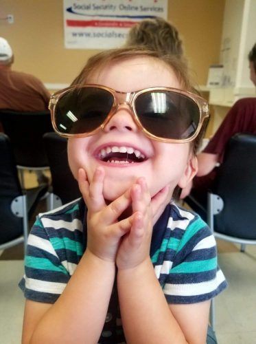 A little boy wearing sunglasses is smiling in front of a sign that says social security online service