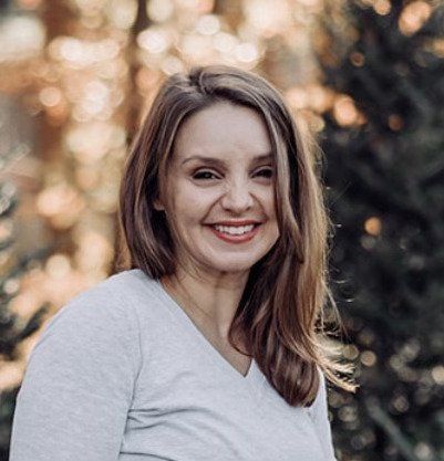 A woman in a grey shirt is smiling for the camera.