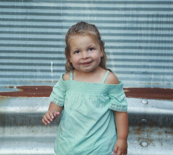 A little girl in a green dress is standing in front of a metal wall.