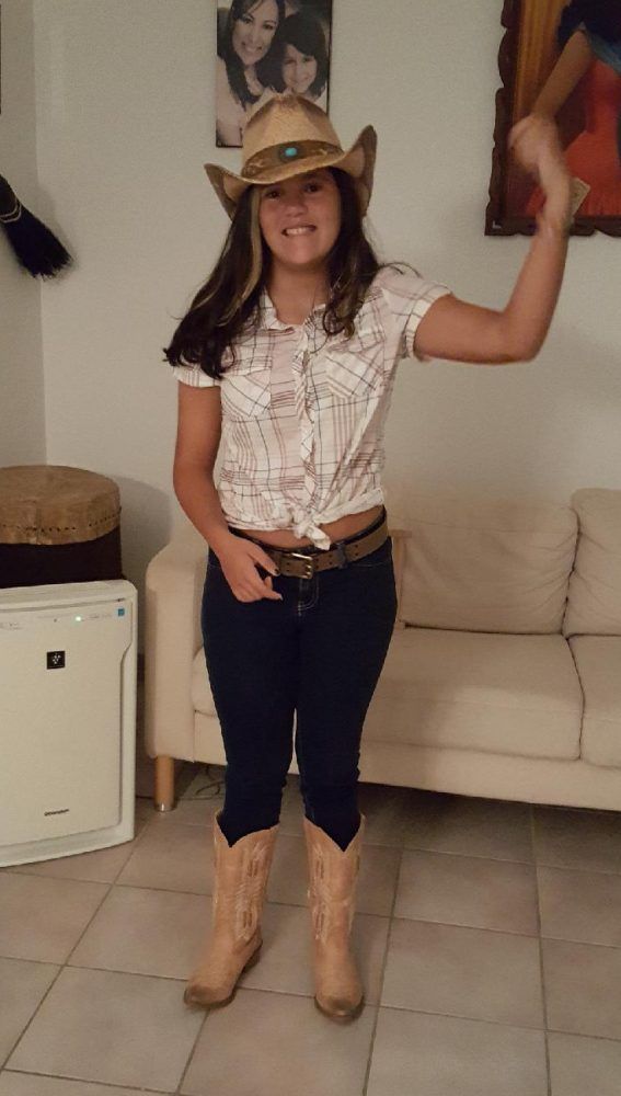 A woman wearing a cowboy hat and cowboy boots is standing in a living room.
