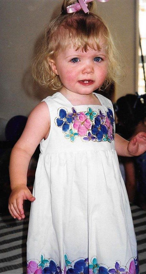 A little girl wearing a white dress with flowers on it.
