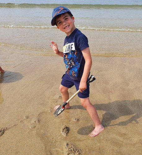 A young boy is standing on the beach holding a shovel.