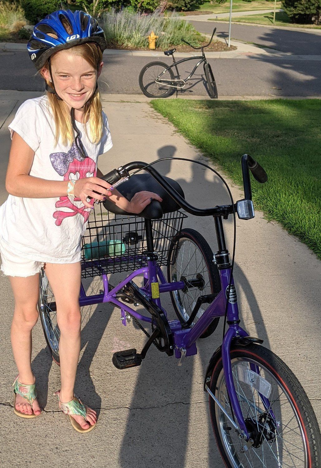 A young girl wearing a helmet is standing next to a purple bicycle.