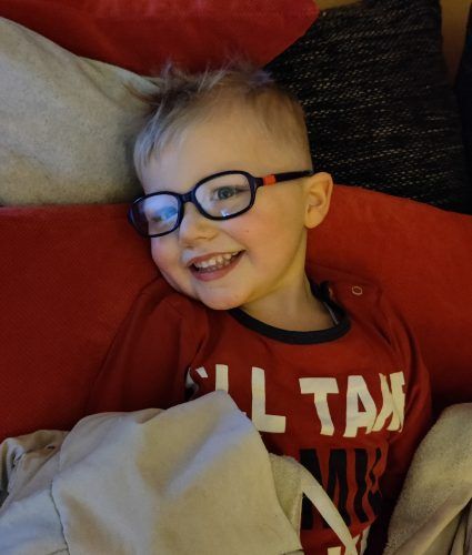 A young boy wearing glasses and a red shirt that says all tax.