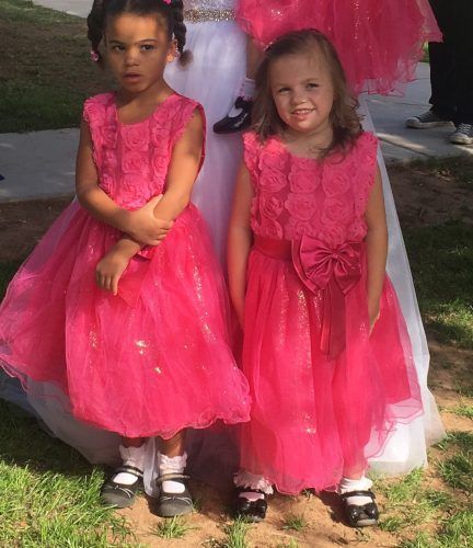 Two little girls in pink dresses are standing next to each other