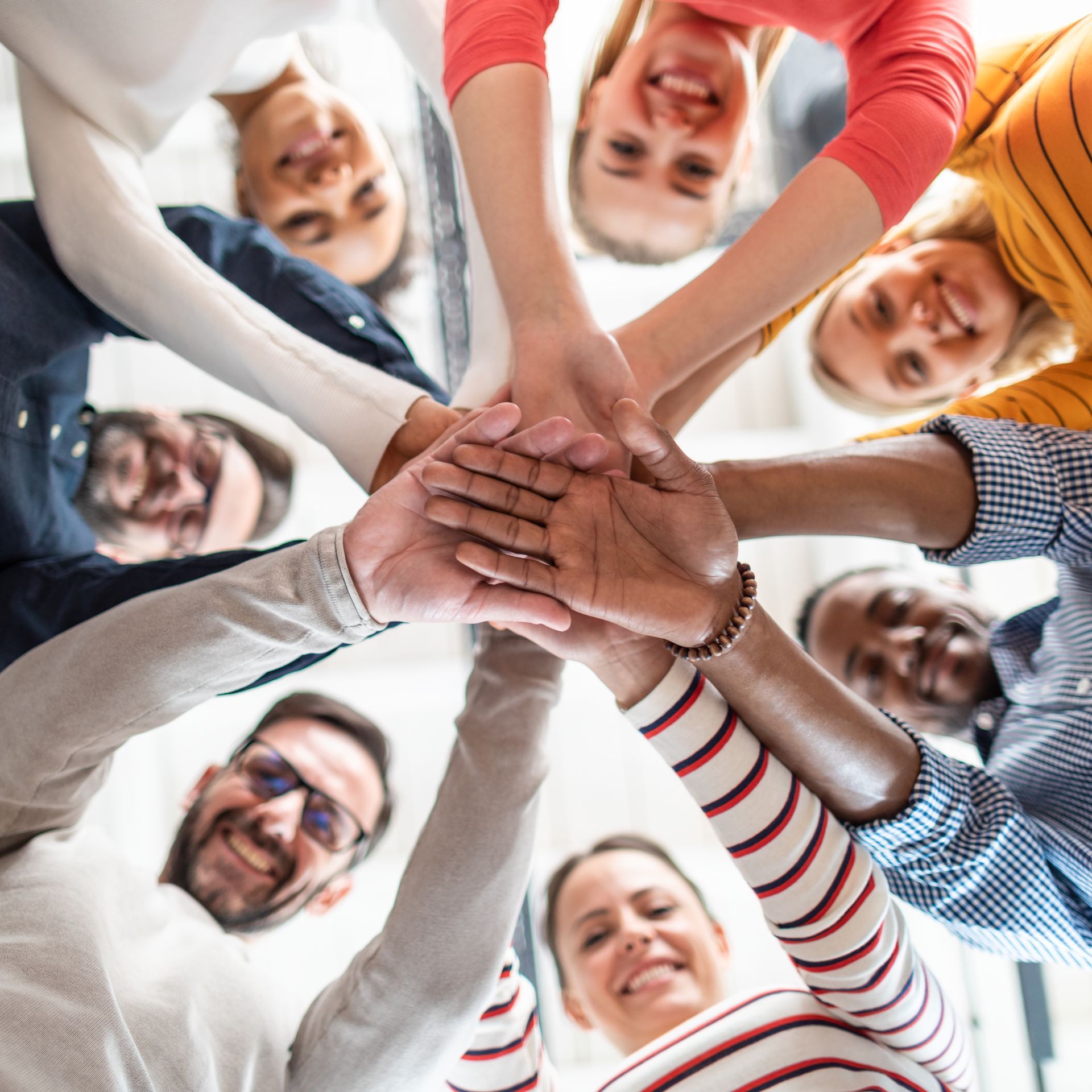 Group of diverse people with hands in a circle, smiling, demonstrating teamwork and unity.