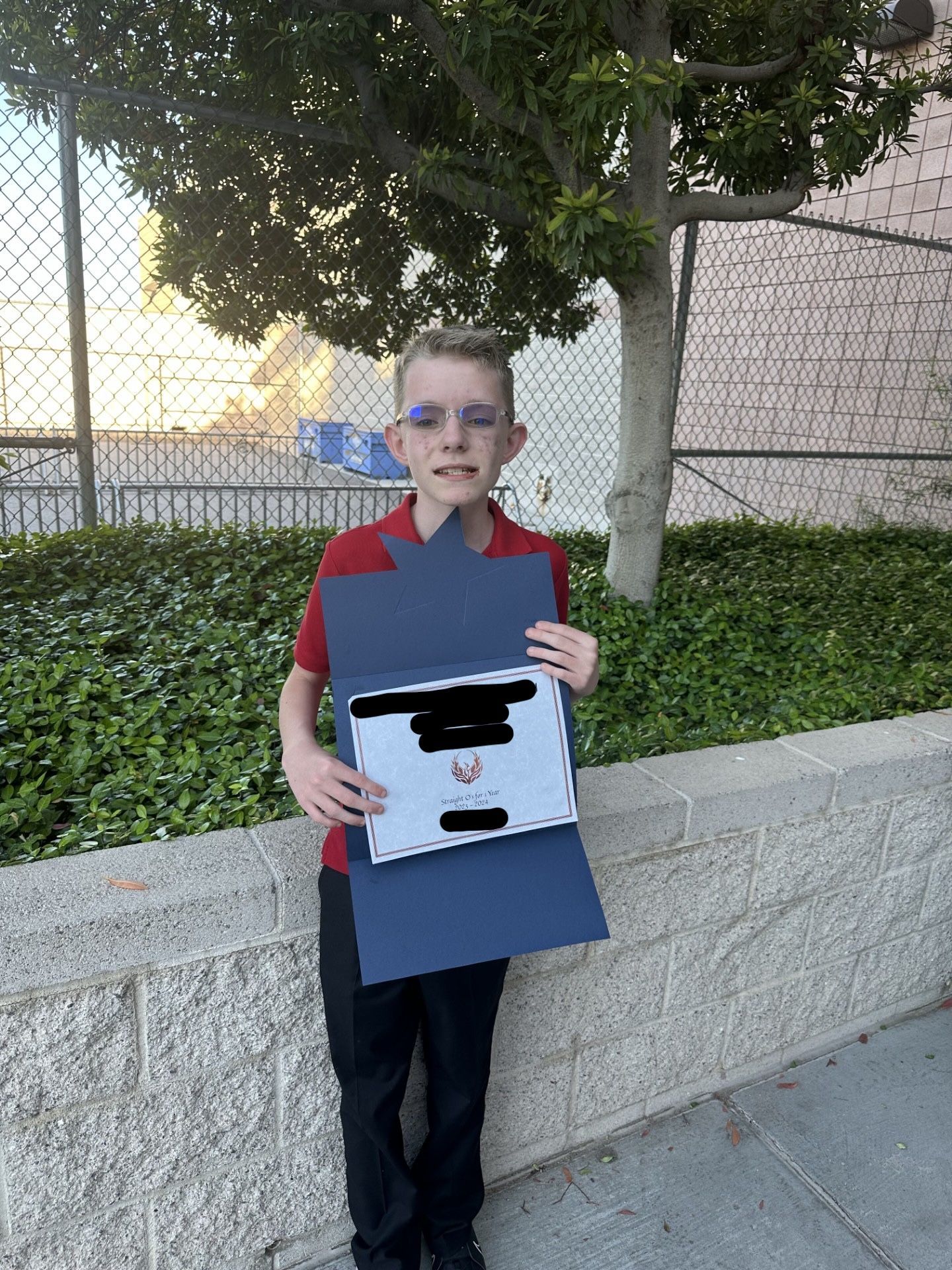 A young boy is holding a piece of paper in front of a tree.