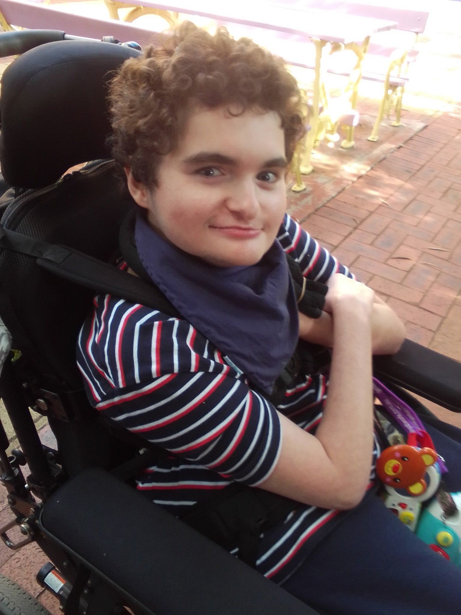 A young boy is sitting in a wheelchair and smiling at the camera.